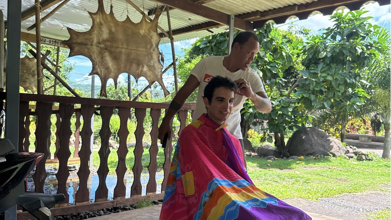 Andrés getting his haircut in a carport in front of a goat hide