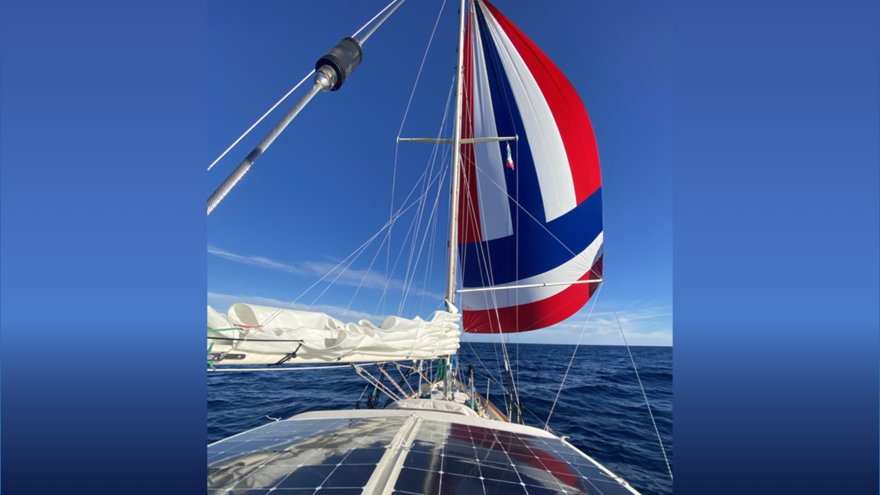 Ana Maria sailing under her red, white, and blue spinnaker with the solar panels in the foreground